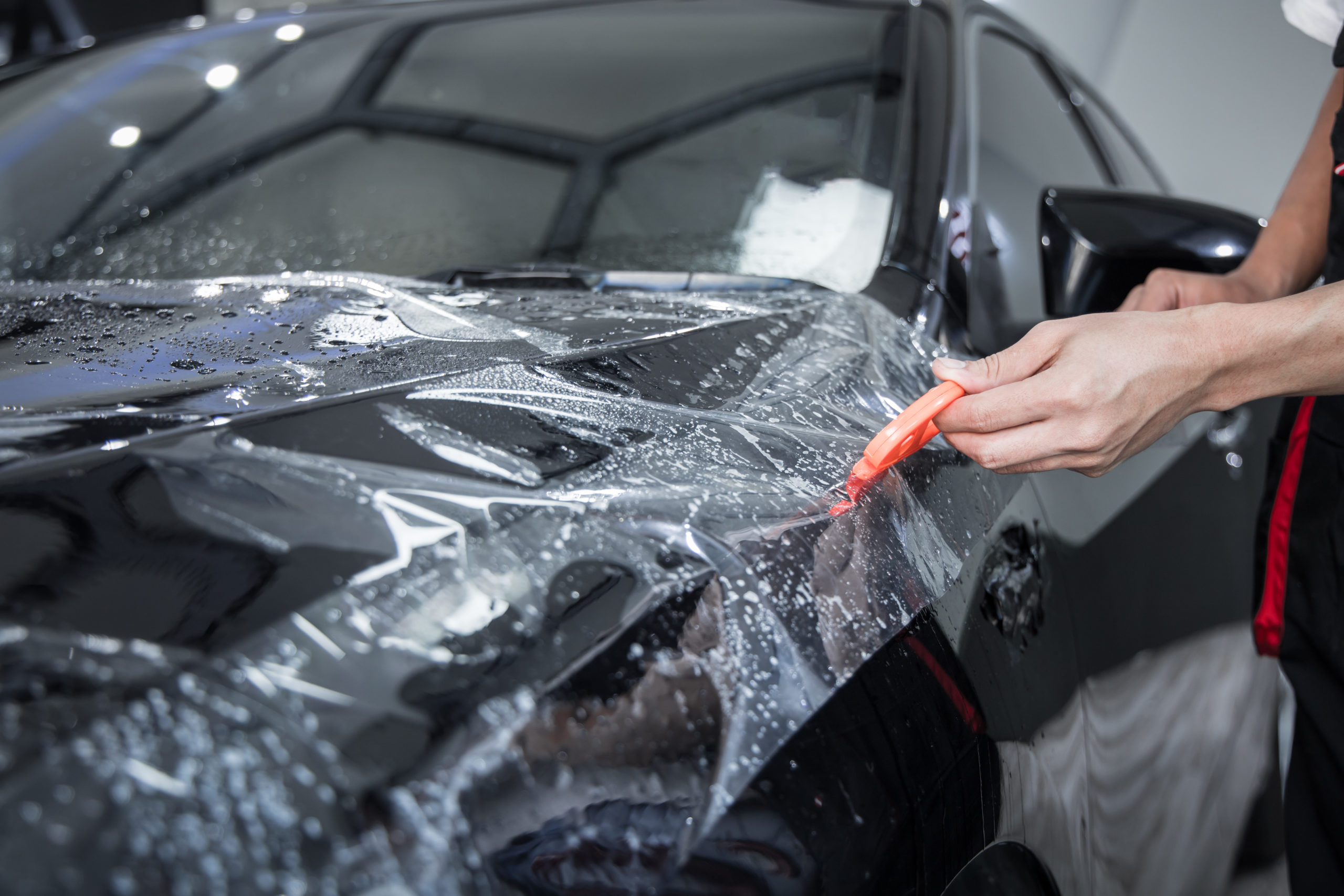 Mechanic with transparent film, car paint protection. Mechanic installs car paint protection film. Install car paint protection film. Car wrap concept.